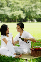 Naklejka premium Couple sitting with picnic basket, smiling at each other, man pouring wine from bottle