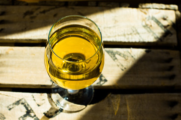 Glass of white Muscat wine with rich yellow ochre copper glow on a wood box in sunrays