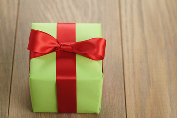 green paper gift box with classic red ribbon bow on wooden table