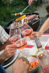 Happy friends having fun outdoors, hands toasting rose wine glass