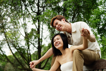 Fototapeta premium Couple sitting on park bench, man sitting behind woman, holding her hands