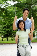 Woman sitting on swing, man behind her, smiling at camera