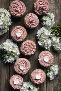 Overhead view of pink iced cupcakes on a wooden board with flowers
