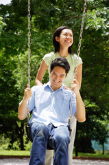 Man sitting on swing, woman standing behind him