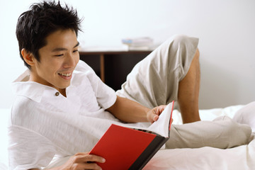 Man lying on bed, reading book, smiling