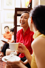 Women sitting, smiling, holding cups and saucers