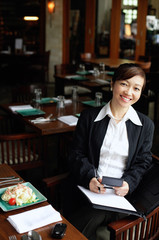 Businesswoman in restaurant, holding pen and folder, smiling