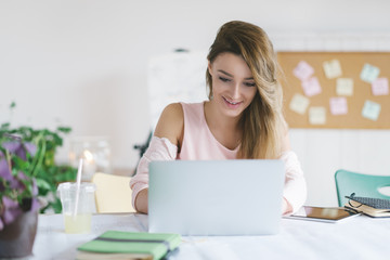 Young smiling businesswoman working in her office and typing on her laptop.