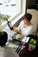 Women in restaurant, food on the table, one woman holding bottle of wine