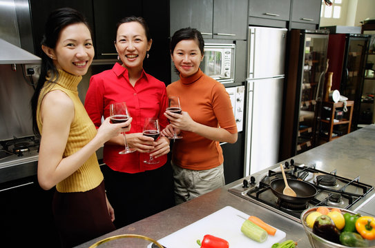 Three women in kitchen, holding wine glasses, smiling at camera