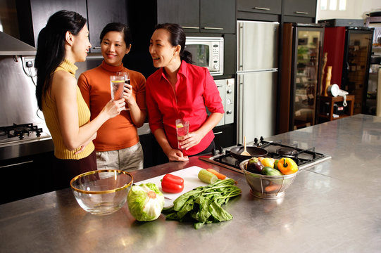Three women in kitchen, holding wine glasses, talking