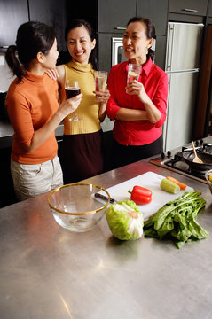 Women in kitchen, standing side by side, holding drinks