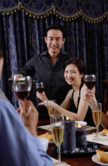 Couples at home around dinner table, man pouring wine for woman, smiling at camera