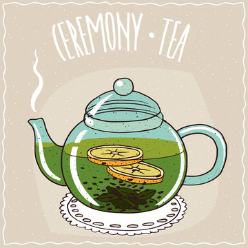 Fototapeta Transparent glass teapot with hot brewed green tea with lemon, lie on a lacy napkin. Beige background and ornate lettering Ceremony tea. Handmade cartoon style