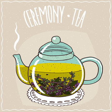 Fototapeta Transparent glass teapot with hot brewed tea with thyme, lie on a lacy napkin. Beige background and ornate lettering Ceremony tea. Handmade cartoon style