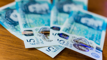 New Five Pound Notes on a wooden table F Shallow Depth of Field, new polymer note, introduced in September 2016