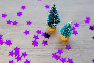 two little green Christmas trees as a symbol of the new year on wooden background with purple stars, tinsel, top view, there is a place for the text as a background and substrate