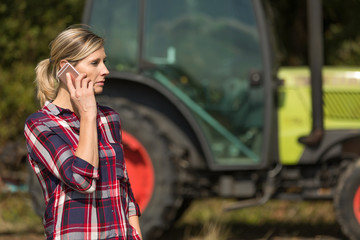 female farmer with tractor using mobile phone