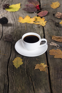 white cup of coffee on a wooden background with autumn leaves