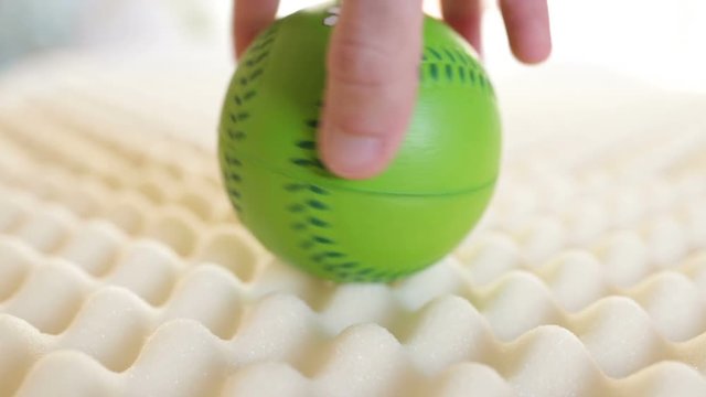 Testing the Memory Foam Bed Mattress with a Green Soft Ball pressed by the hand of a man.