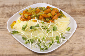 Mashed potatoes with fried carrots, peas and fresh sunflower sprouts. Dish on a wooden table. 