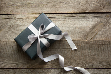 Gift box wrapped in black paper with silver ribbon on wooden surface.