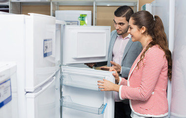 Young smiling couple looking at large fridges