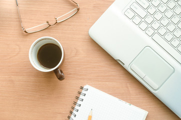 Laptop, cup of coffee, glasses and notebook on the desktop