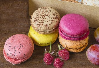 Multicolored french macaroons, cup of black coffee, several purple flowers and berries on old wooden background
