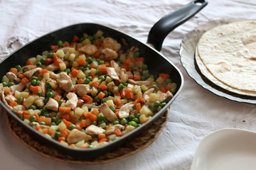 Chicken and mixed vegetables (potato, carrot, peas) cooked in a cooking pan and tortillas. Selective focus. 