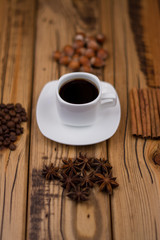Small white cup of coffee, cinnamon sticks, cocoa beans, star anise, hazelnuts on wooden background