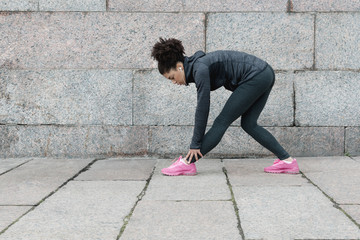 Female runner doing warm up exercise before training on city street