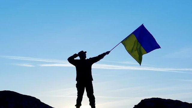  Soldier  salute Ukrainian Flag  against blue sky .Slow  motion