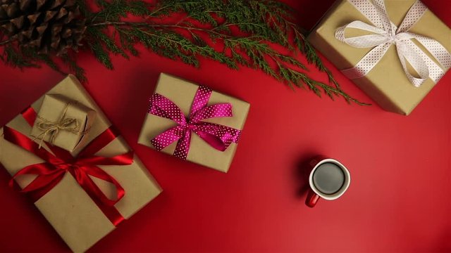 Top view hands drinking coffee christmas presents table on red background from above.