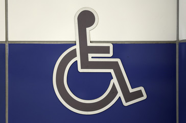 Grey wheelchair sign on the a white and blue wall. Public restroom signs with a disabled access symbol.