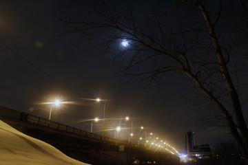 Fototapeta na wymiar Night lights on the bridge and snow on the river