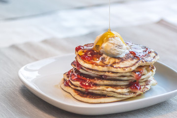 Pancakes with vanilla ice cream strawberry jam and maple syrup with selective focus in white plate with light brown cover. Concept for family breakfast.