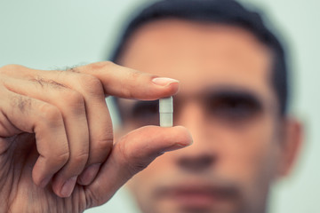 Man holding white capsule. Face in the background blurry. Concept for medicine, choice.