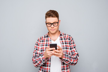 Young handsome man in glasses typing sms on gray background