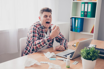 Young businessman with grippe working on laptop and sneezing in