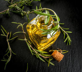Rosemary essential oil jar glass bottle with branches of plant rosemary, on black table, close top view