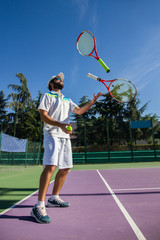 Fototapeta na wymiar Professional tennis player juggling with rackets. He is having a good time before starting the game. 