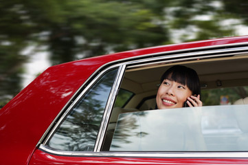 Woman sitting in car, using mobile phone, smiling