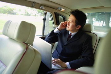 Businessman in car, using laptop and mobile phone