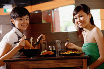 Two young women sitting at table in restaurant, smiling at camera