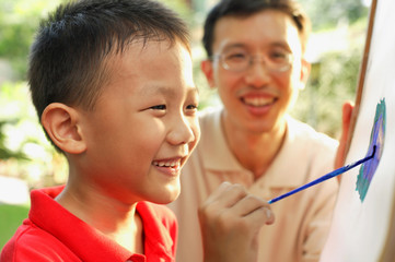 Boy drawing on easel, father watching