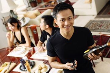 Man looking at camera, holding wine bottle, people in the background