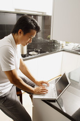 Man sitting at kitchen counter, using laptop