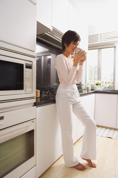 Young woman standing in kitchen, drinking coffee