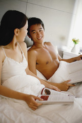 Couple sitting up in bed, holding book and magazine